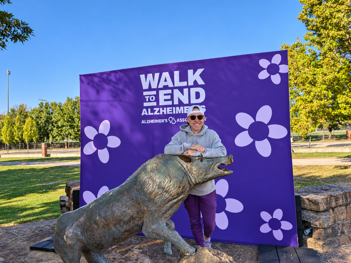 Brock Short beside the Razorback statue in front of the purple Walk to End Alzheimer’s backdrop at the University of Arkansas