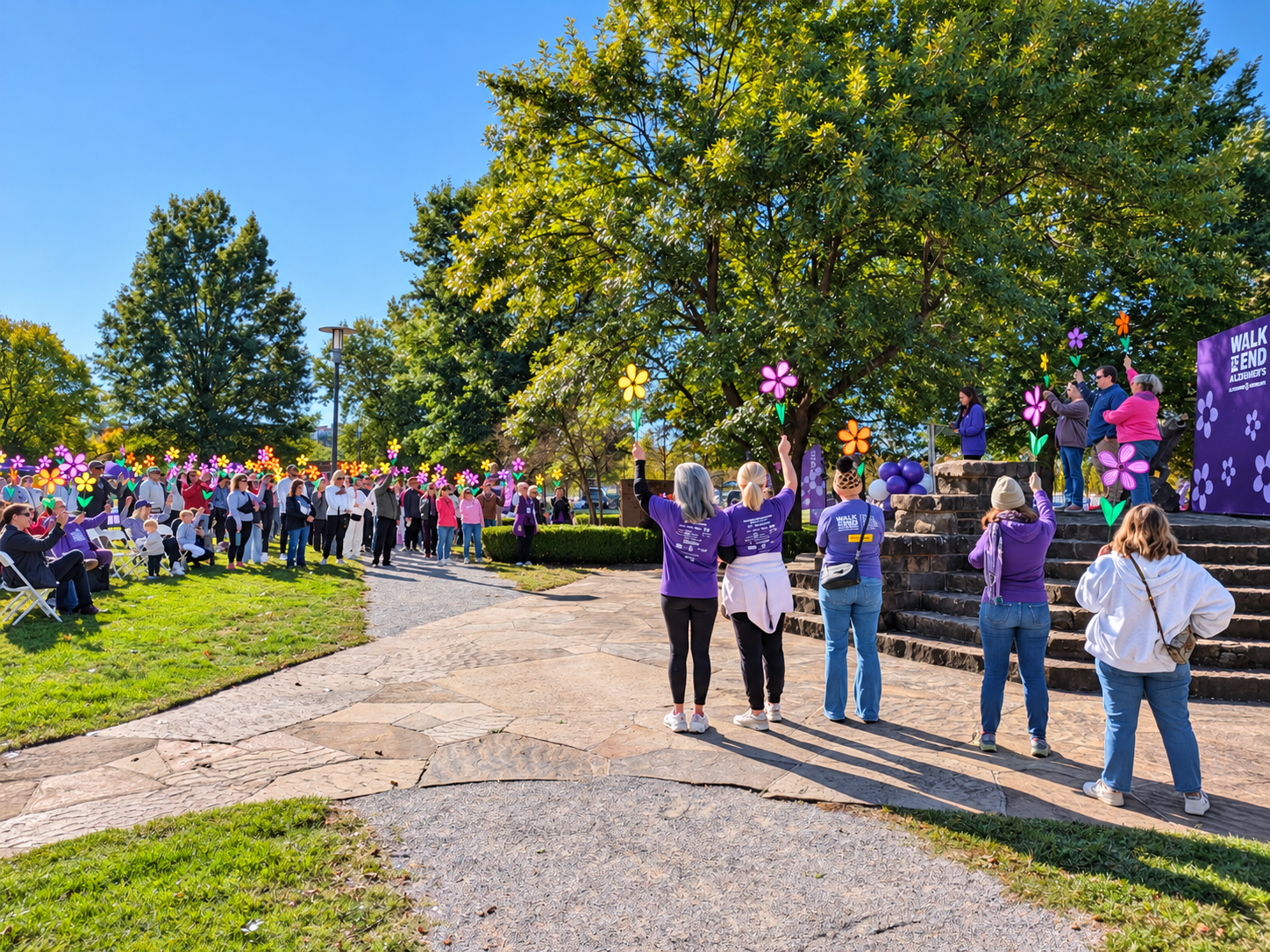 Participants raise colorful flowers during the Walk to End Alzheimer’s ceremony at Razorback Gardens on the University of Arkansas campus in Fayetteville