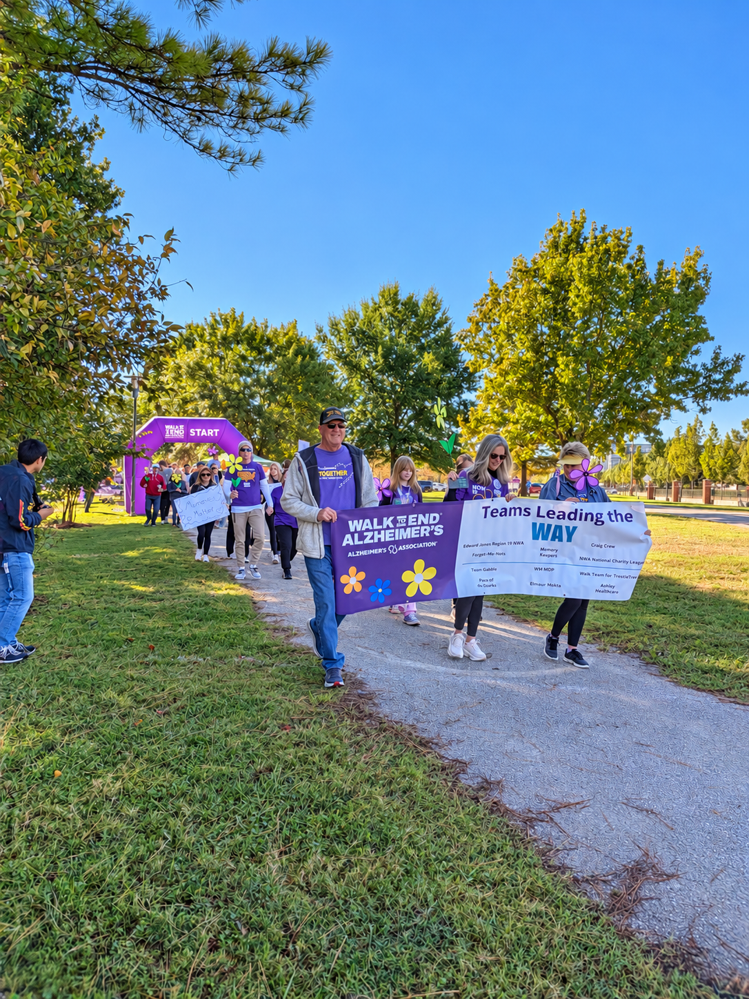 Walk participants carry the Teams Leading the Way banner along the path at Razorback Gardens in Fayetteville